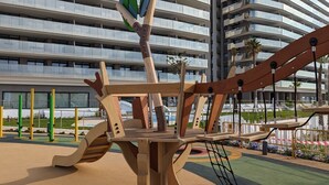 Un parque infantil con estructuras de madera para escalar y un edificio con varios balcones al fondo.