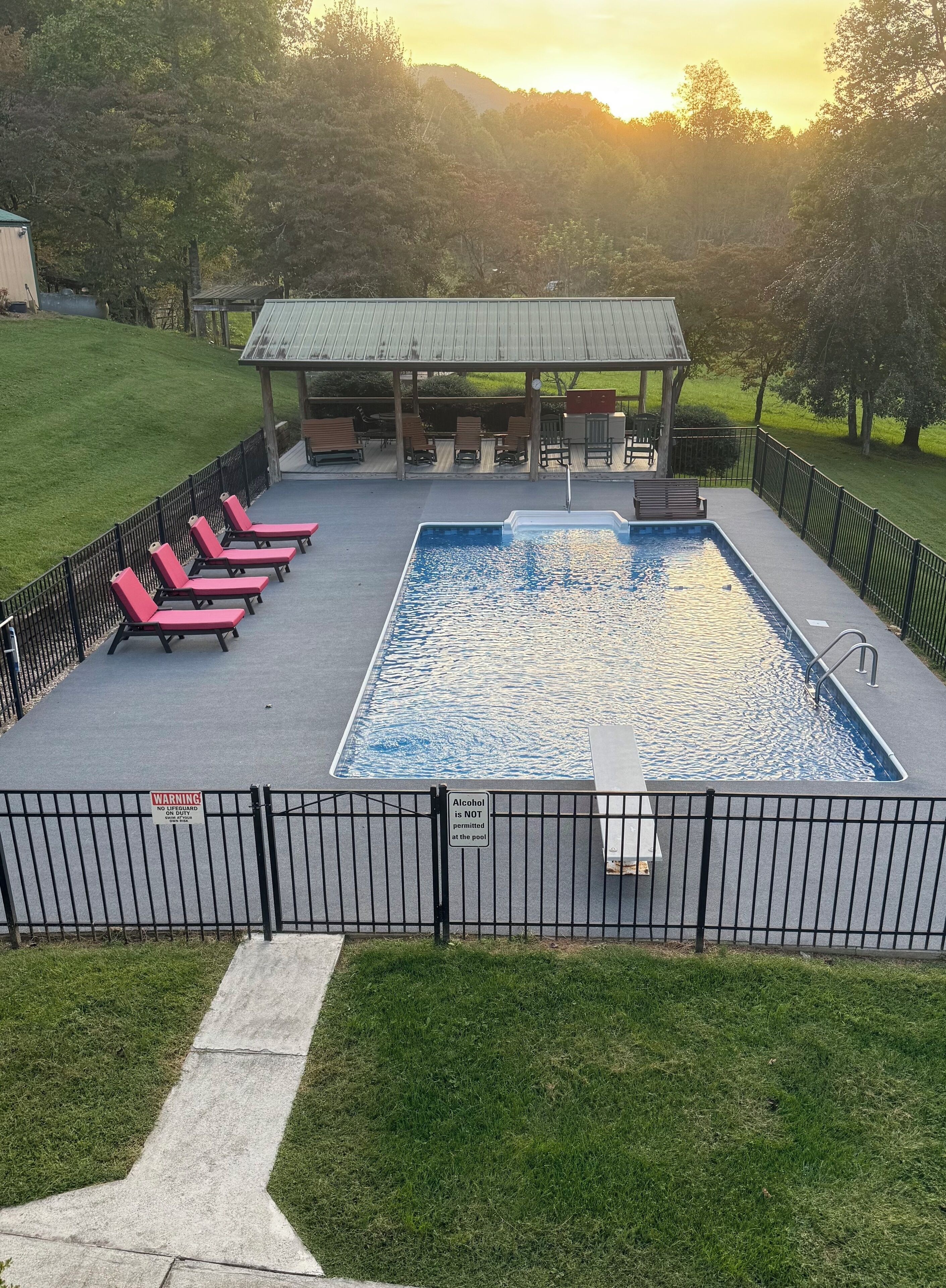 A swimming pool with a fenced deck, lounge chairs, and a covered seating area.