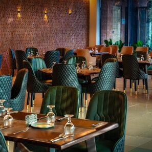 A restaurant with green upholstered chairs, wooden tables, and a brick wall in the background. - Hotel Park Valley International (Dhaka)
