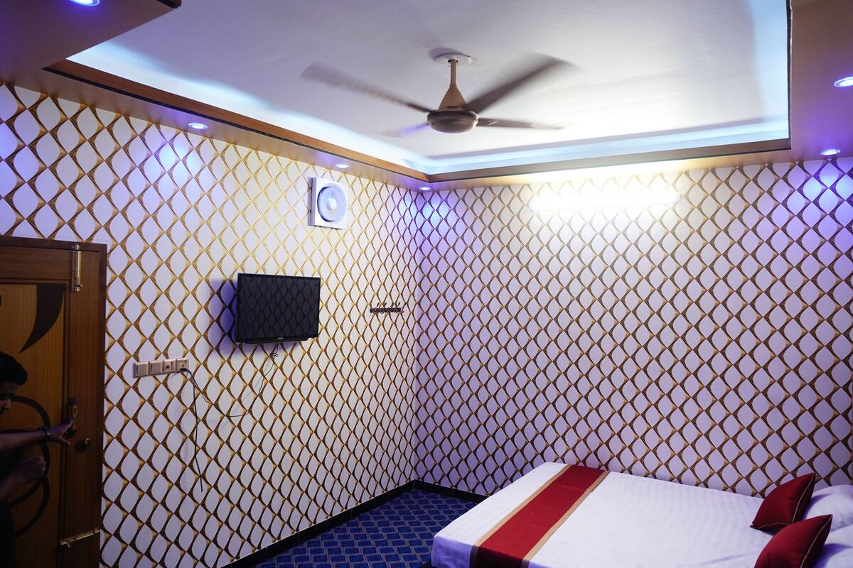 Una habitación de hotel con pared estampada, cama con ropa de cama roja y blanca, ventilador de techo y televisor montado en la pared.