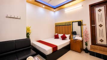 A hotel room with a bed, a sofa, a small table with a vase, a mirror, and a wooden door.