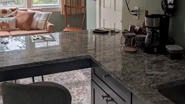 A modern kitchen with a large island, a flat-screen TV mounted above the island, and a dining area with a sofa and curtains. - 1880 updated Victorian 1st floor, water views (Salem)