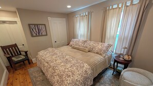 A bedroom with a large bed, a chair, a small table, and a window with curtains. - 1880 updated Victorian 1st floor, water views (Salem)