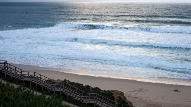 A beach with a wooden staircase leading down to the shore, a sandy beach, and the ocean.