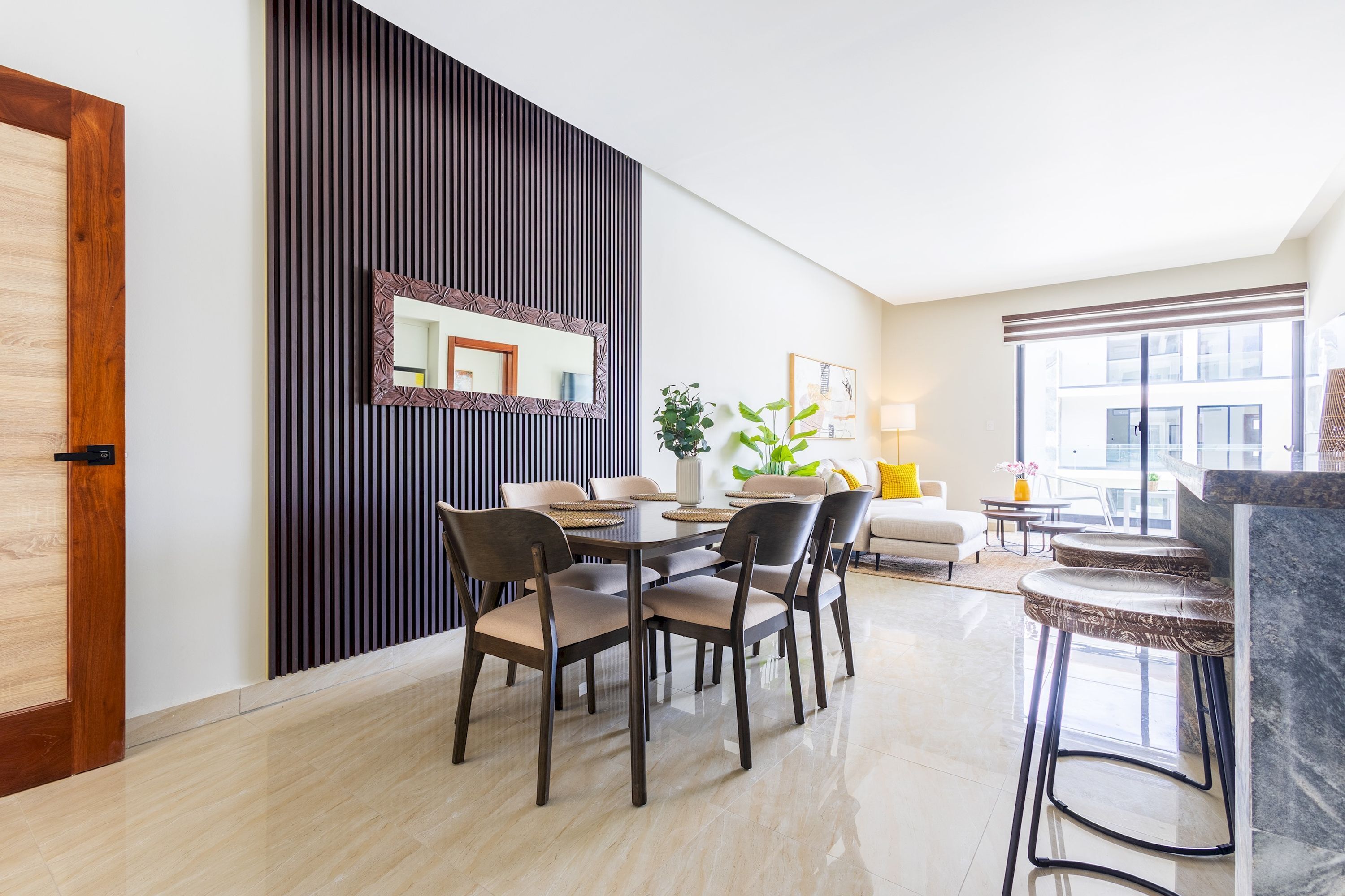 Een moderne eetruimte met een ronde tafel, zes stoelen, een decoratieve spiegel en een potplant.
