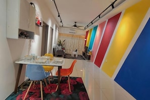 A dining area with a table set for two, chairs, and a small table with a plant.