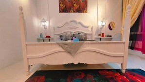 Une chambre à coucher avec un lit blanc, un tableau au-dessus du lit et une lampe sur la table de chevet.
