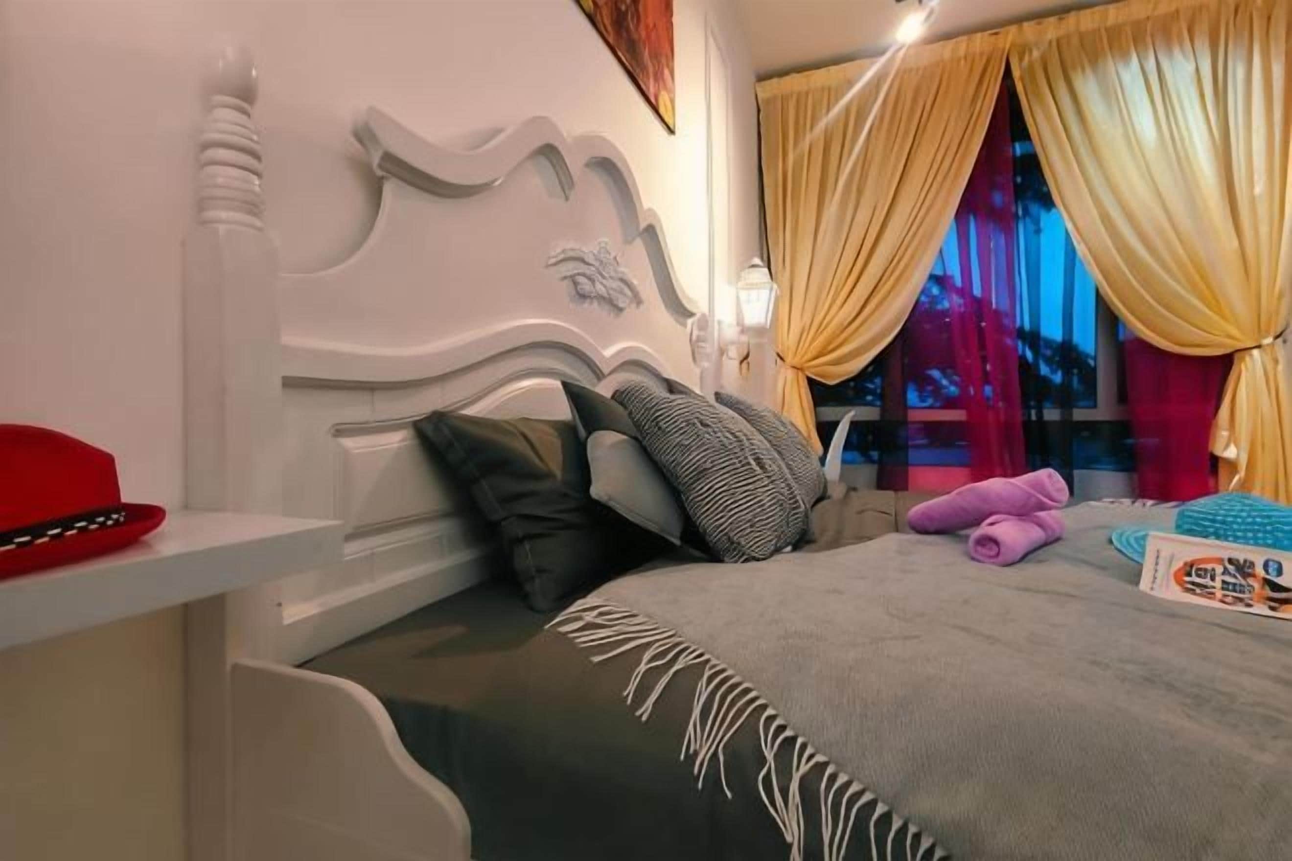 Un letto con testiera, cuscini, coperta e una finestra con tende.