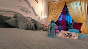 Een bed met kussens, een nachtkastje met een lamp en een raam met gordijnen.
