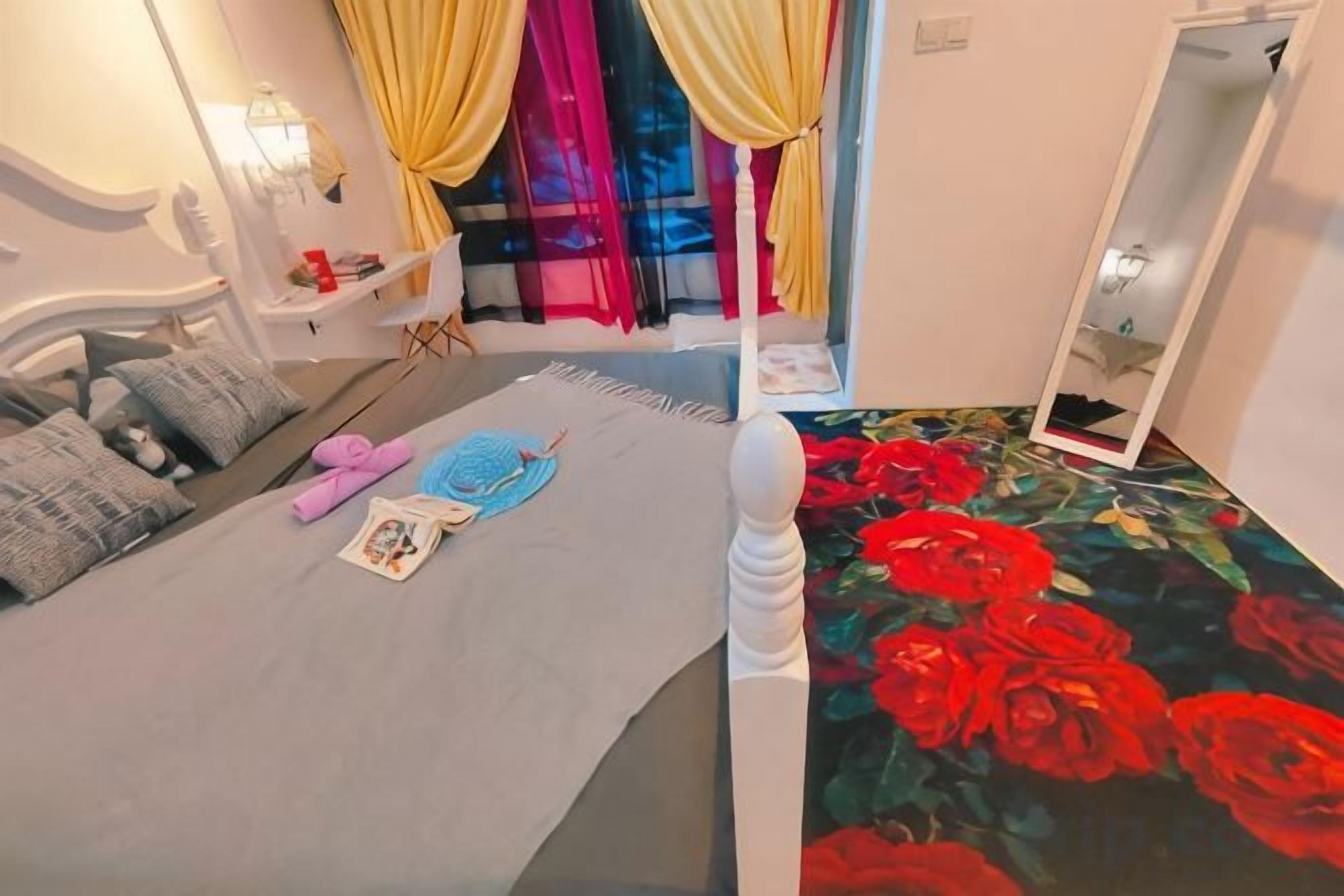 A bedroom with a bed, a bedside table, a mirror, and a window with curtains.