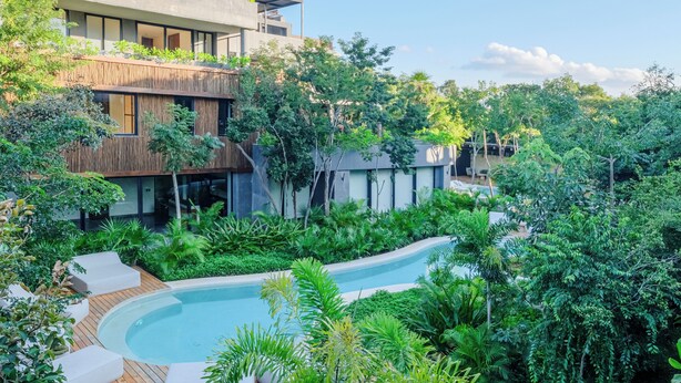 A modern building with a pool surrounded by lush greenery. - 2-bedroom condo in enchanting Tulum with AC (Tulum)