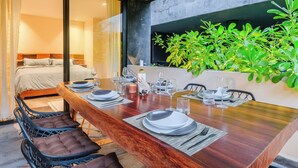 A dining area with a wooden table set for four, a bed with a view, and a green plant wall. - 2-bedroom condo in enchanting Tulum with AC (Tulum)