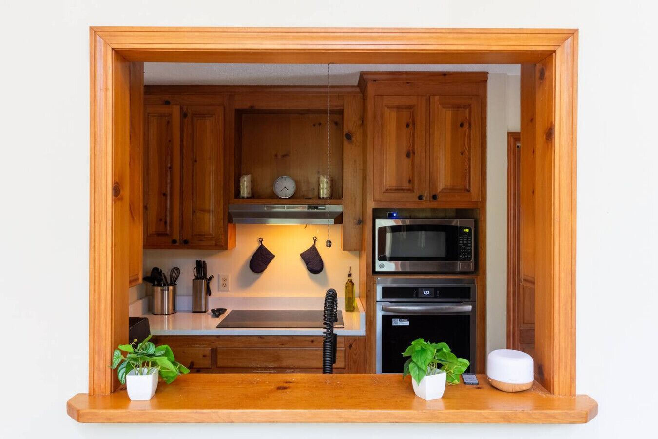 A compact kitchen with wooden cabinets, a microwave, an oven, and a sink. There are two potted plants on the counter.