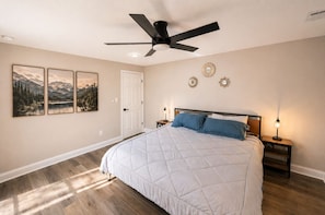 A bedroom with a bed, a ceiling fan, a nightstand with a lamp, and wall art. - Walk 2 Helen, Spacious Cabin for 12|Pet (Helen)
