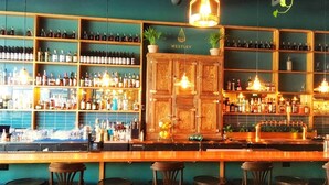 A bar area with wooden shelves stocked with various bottles, a bar counter, and several stools.