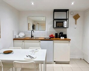 A compact kitchen with a white countertop, a microwave, and a sink. There is a dining table with chairs and a small refrigerator.