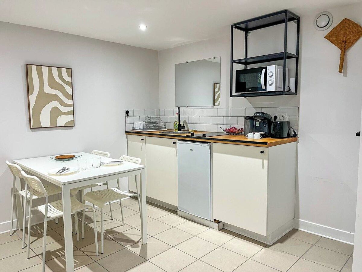 Cocina compacta con una mesa blanca, sillas, microondas y cafetera.