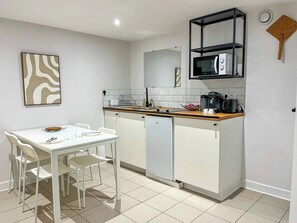 A compact kitchen with a white table, chairs, a microwave, and a coffee maker.