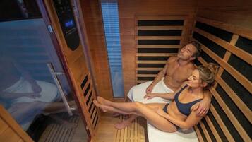 A sauna room with wooden walls and benches, a control panel, and a person lying on a bench.