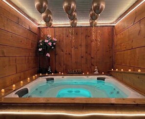 A wooden room with a hot tub, candles, and balloons.