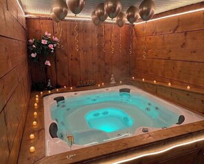 A hot tub with a wooden interior, surrounded by candles, and a statue.