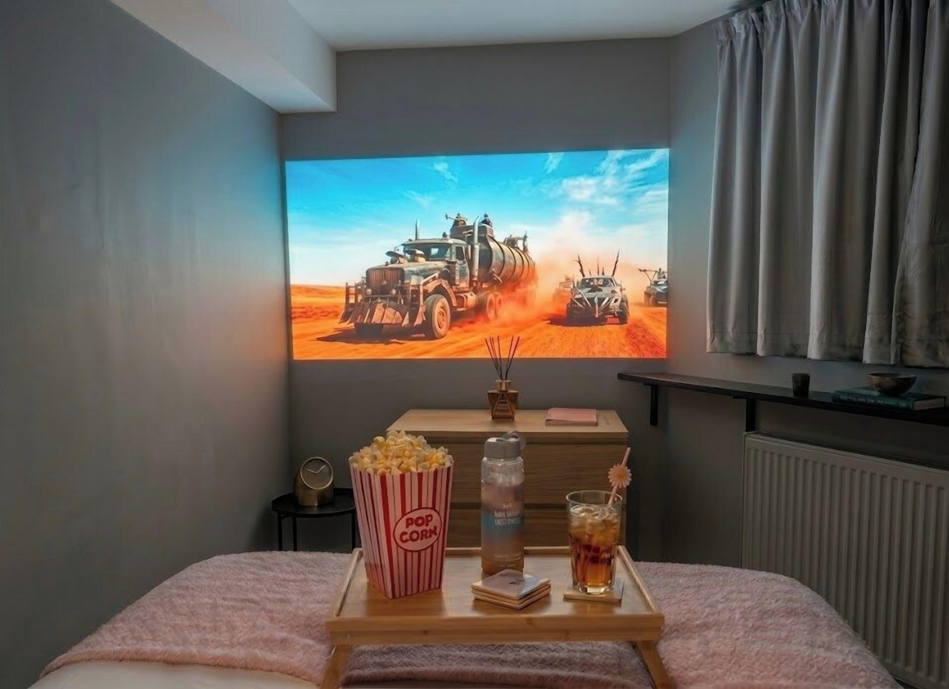 Ein gemütliches Zimmer mit einem Bett, einem Fernseher, der eine Wüstenszene zeigt, einem Tablett mit Snacks und Getränken und einem Fenster mit Vorhängen.