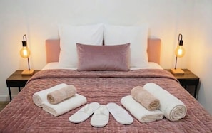 A neatly made bed with a pink quilt, two pillows, and a pair of slippers and towels on the bed. - L'évasion : Jacuzzi & Sauna (Tassin-la-Demi-Lune)
