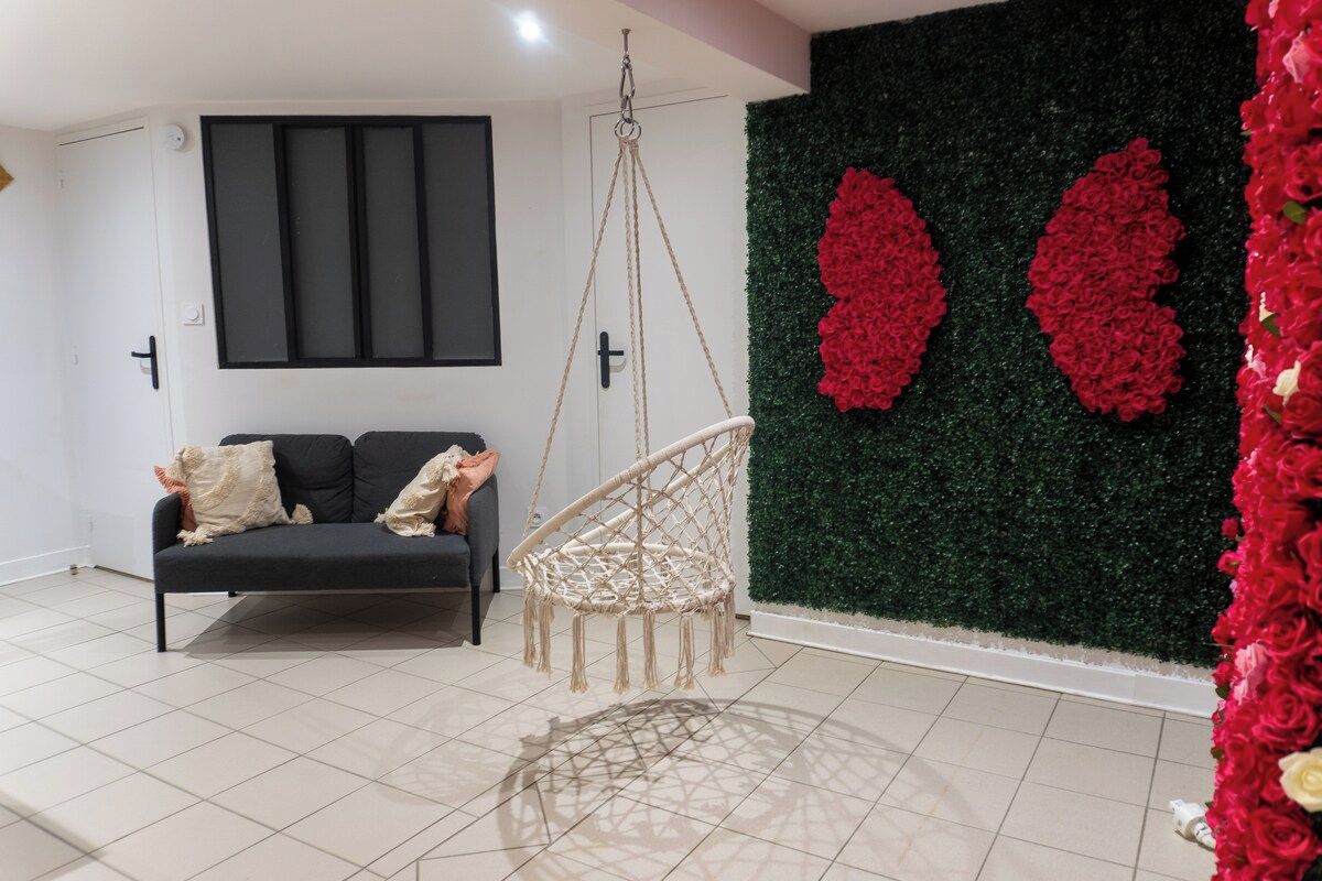 Una habitación moderna con un sofá negro, una silla de macramé y una pared decorada con flores rojas.