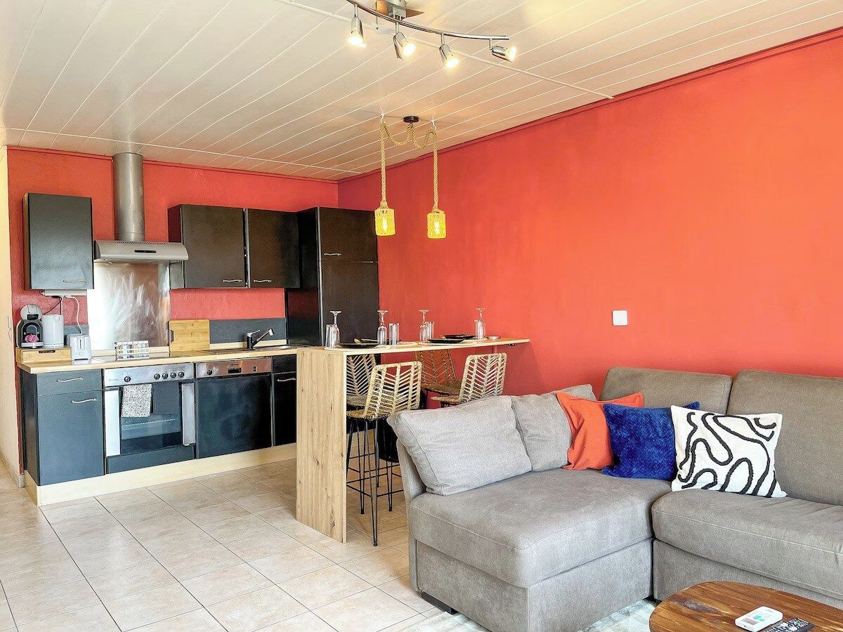 Un espacio habitable compacto con kitchenette, comedor y zona de estar con sofá y sillas.