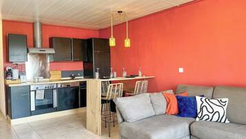 Un espacio habitable compacto con kitchenette, comedor y zona de estar con sofá y sillas.