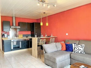 Een compacte leefruimte met een kitchenette, een eethoek en een zithoek met een bank en stoelen.
