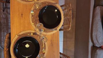 A wooden dining table with multiple black plates and gold cutlery, surrounded by wicker chairs.