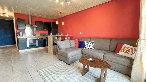 Ein Wohnzimmer mit einer Couch, einem Couchtisch und einer Küchenzeile im Hintergrund.