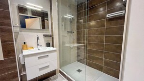 Ein modernes Badezimmer mit einer gläsernen Duschkabine, einem weißen Waschtisch mit Spiegel und einem gefliesten Boden.