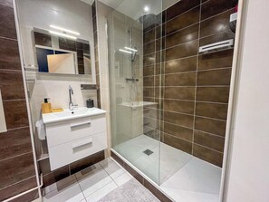 Een moderne badkamer met een douchecabine van glas, een wit wastafelmeubel met spiegel en een betegelde vloer.