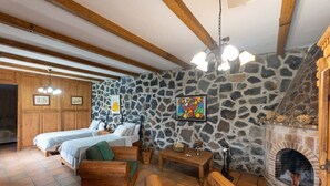 Una habitación rústica con dos camas de madera, un muro de piedra, una chimenea y una mesa de madera.