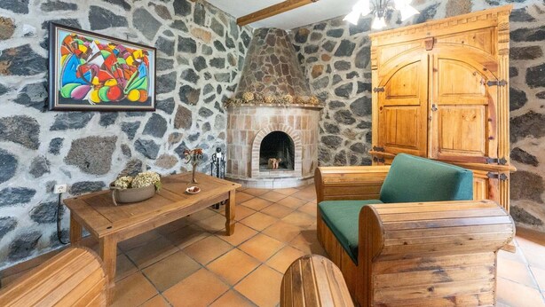 Un interior rústico con una pared de piedra, una chimenea, muebles de madera y un cuadro de colores.
