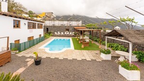 Un área de piscina con muro de piedra, sillas de descanso y una pérgola.