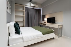 A modern hotel room with a bed, a desk, a television, and a wardrobe.