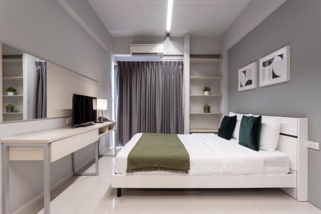 A modern bedroom with a bed, a desk, a TV, and a mirror.