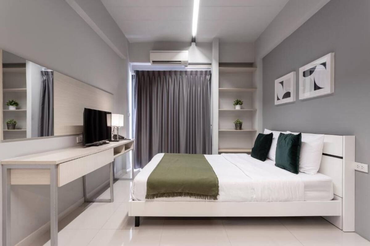 A modern bedroom with a bed, a desk, a TV, and a mirror.