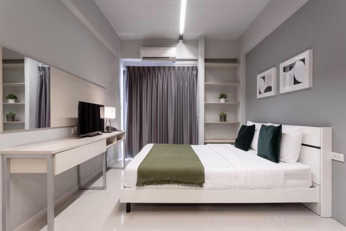 Een moderne slaapkamer met een bed, nachtkastjes, een bureau, een spiegel en een televisie.