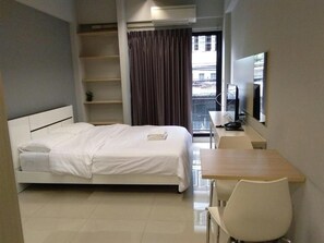 A hotel room with a bed, a desk, a chair, a TV, and a window with curtains.