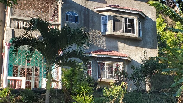 A two-story house with a red-tiled roof, surrounded by lush greenery and trees. - Can sleep 7 people with private parking (Aeolus Valley)