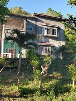 A two-story house with a red-tiled roof, surrounded by lush greenery and trees.