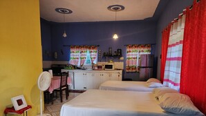 A room with two beds, a small kitchenette, a dining area, and a fan. - Can sleep 7 people with private parking (Aeolus Valley)