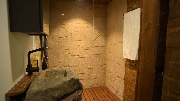 Ein Badezimmer mit Steinwänden, einer hölzernen Sitzbank, einem Handtuch an der Wand und einer Duschkabine.