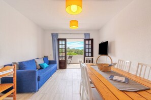 Ein Zimmer mit blauem Sofa, einem Holzesstisch und einem Fernseher an der Wand.