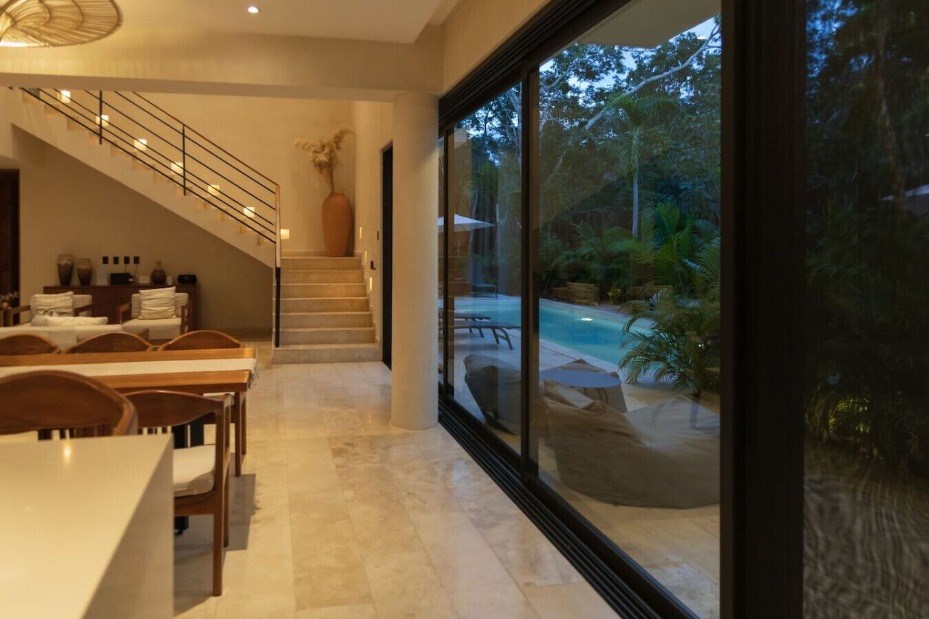 Ein modernes Interieur mit Essbereich, Treppe und großem Panoramafenster mit Blick auf Pool und Garten.