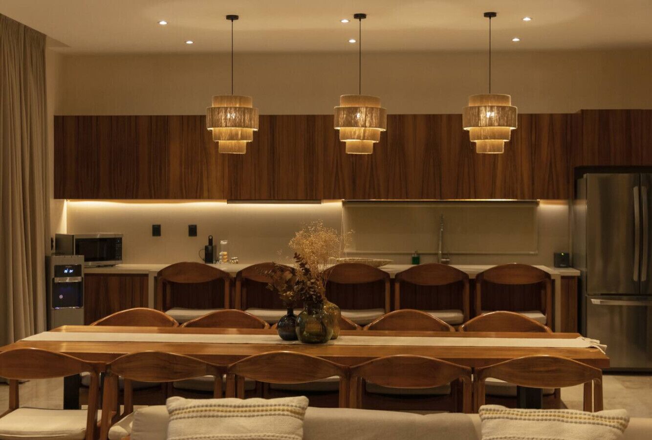 Una cocina moderna con armarios de madera, una mesa de comedor con sillas y lámparas colgantes.
